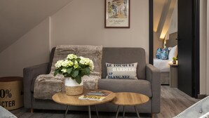 A modern living room with a grey sofa, a small round wooden table, and a vase of flowers.