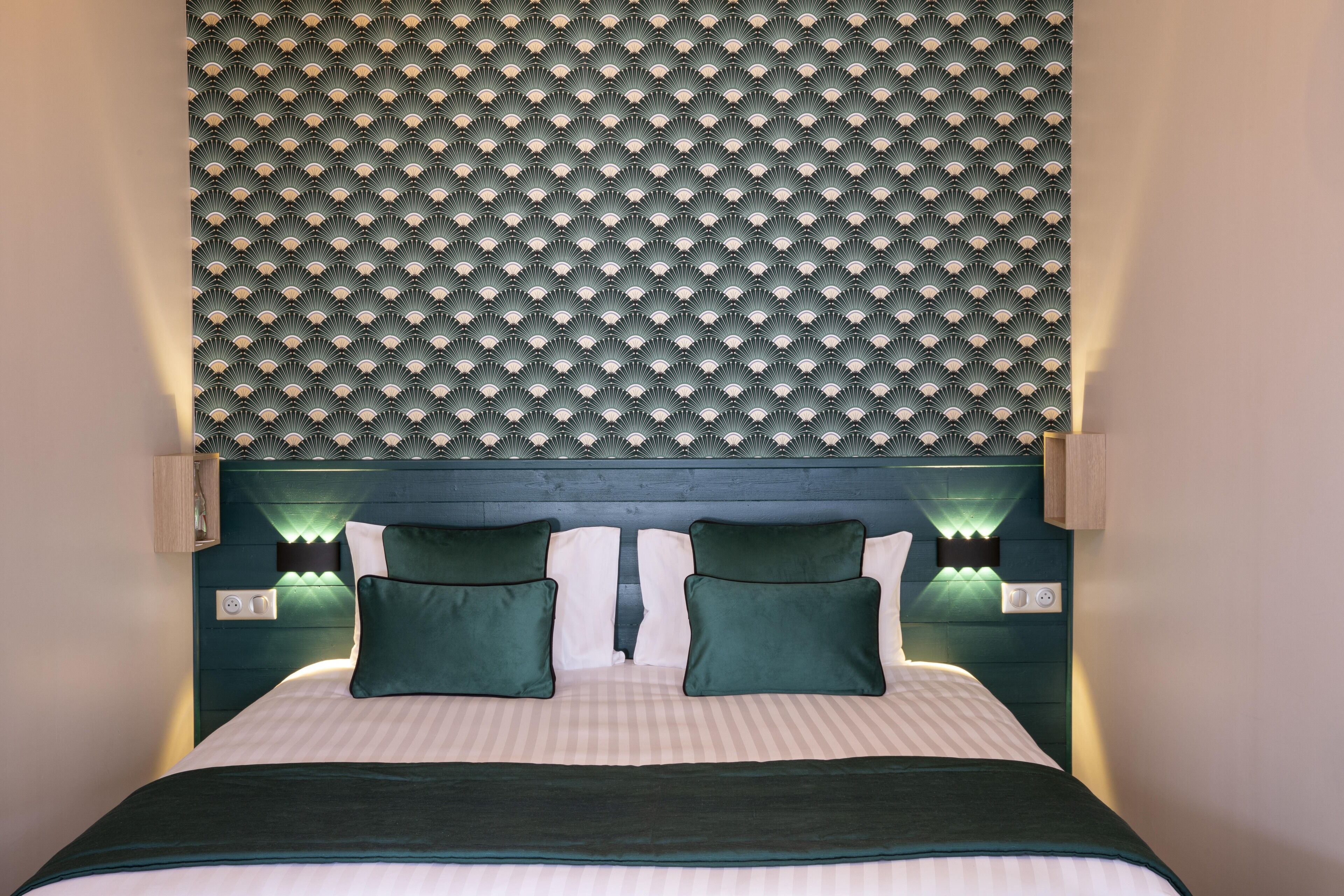 Un lit avec une tête de lit, deux oreillers verts et une couvre-lit à rayures.