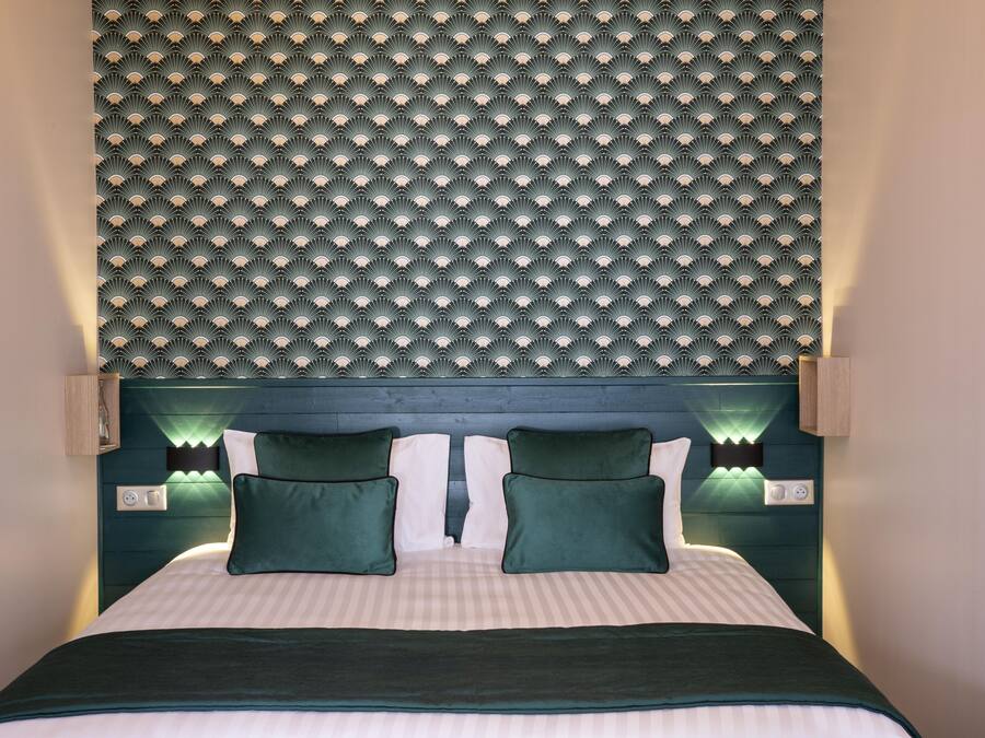 Un lit avec une tête de lit, deux oreillers verts et une couvre-lit à rayures.