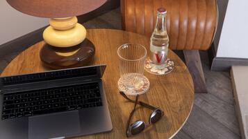 A laptop on a wooden table with a lamp, a bottle, and a glass.