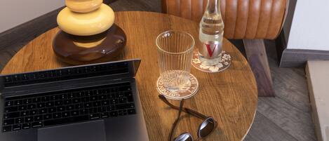 A laptop on a wooden table with a lamp, a bottle, and a glass.