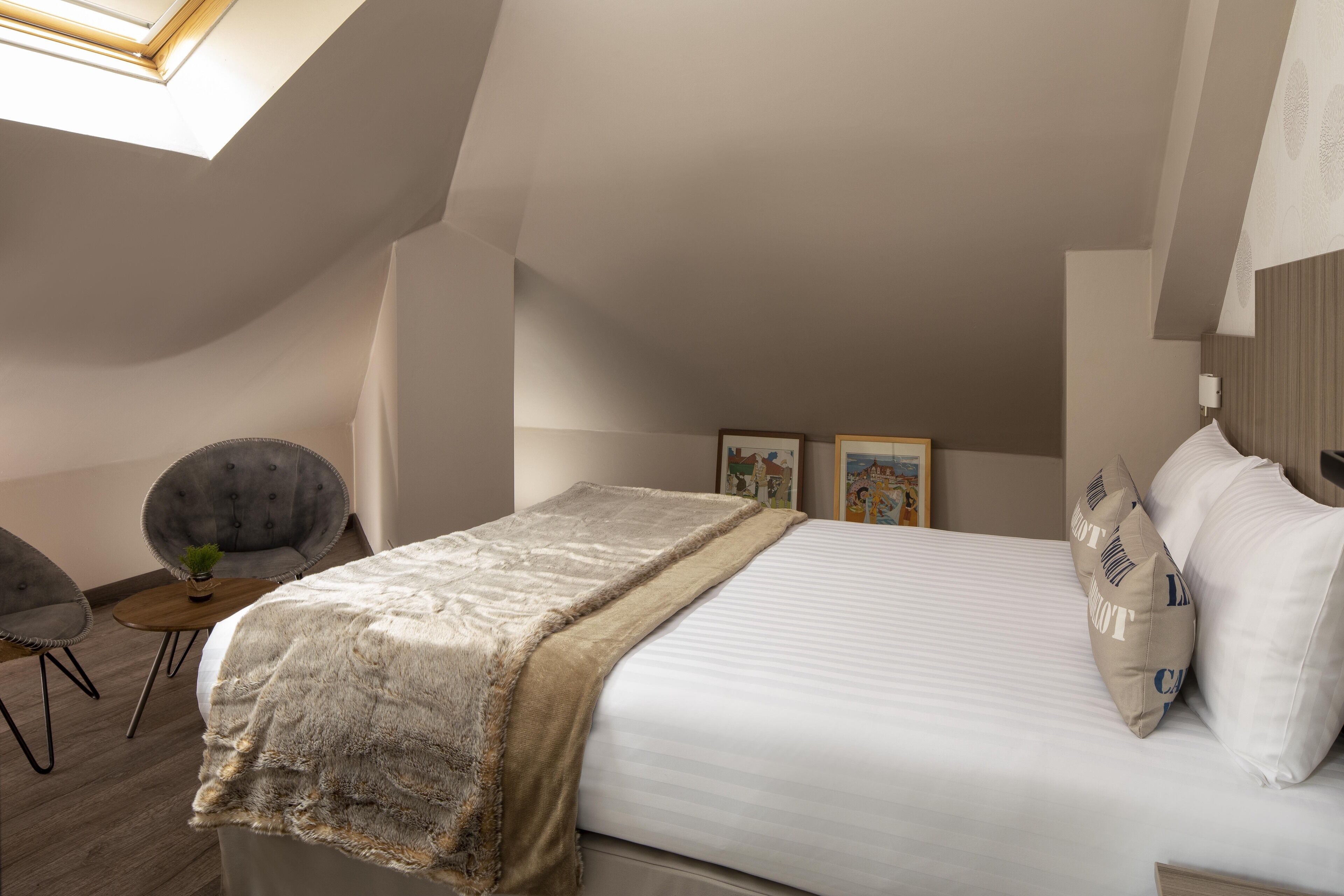 A bedroom with a bed, a chair, a small table, and a picture frame on the wall.