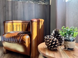 Una habitación moderna con una silla de madera y una mesita de noche de madera. Hay una planta en maceta y una piña en la mesa.