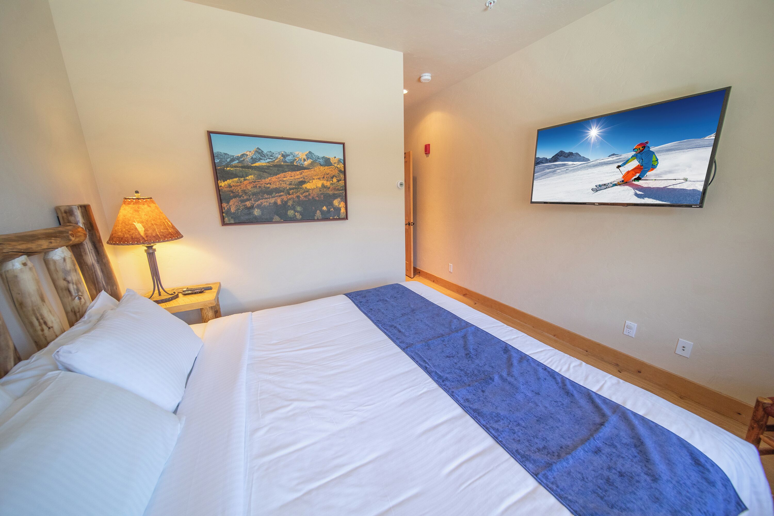 Habitación de hotel con cama, lámpara, un cuadro y una televisión mostrando a un esquiador.