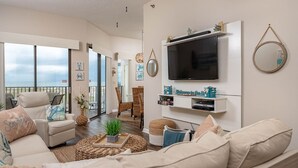 Sala de estar com uma televisão grande, assentos confortáveis e vista para o exterior.