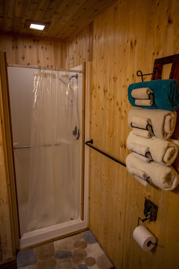 Un baño de madera con cortina de ducha, toallas y un dispensador de papel higiénico.