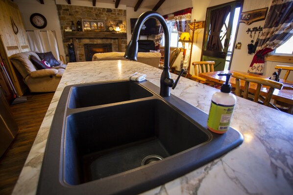 Een keuken met een dubbele spoelbak, een stenen open haard en een eethoek met houten meubels.