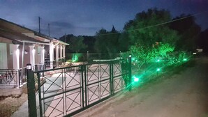 A gated area with a building on the left and a fence with green lights on the right. - Armonia Beach apartment 1 (Δήμος Κορισσίων)