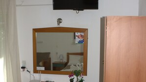 A hotel room with a wooden desk, a chair, a flat-screen TV mounted on the wall, a mirror above the desk, and a wooden wardrobe. - Armonia Beach apartment 1 (Δήμος Κορισσίων)