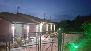 A building with a covered patio area, a fenced outdoor space, and a green fence. - Armonia Beach apartment 1 (Δήμος Κορισσίων)