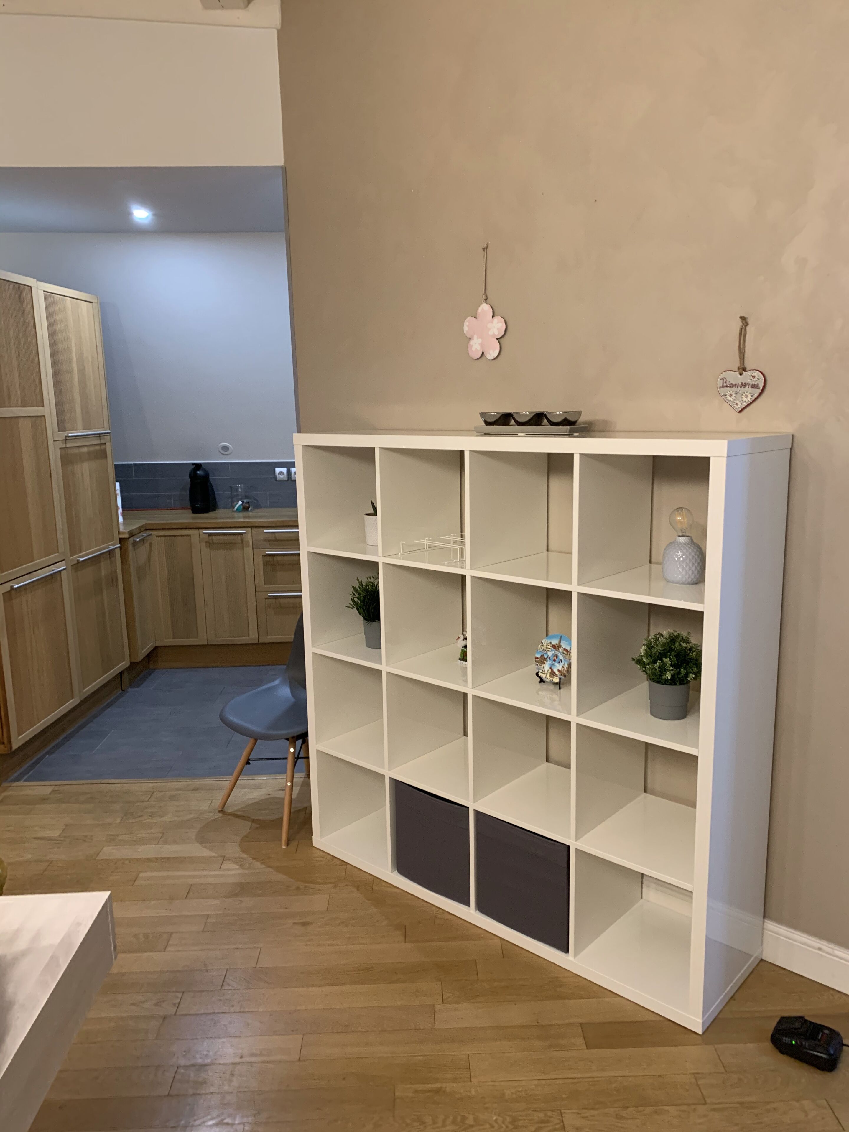 A modern kitchen with wooden cabinets, a white countertop, and a built-in white shelving unit with decorative items.