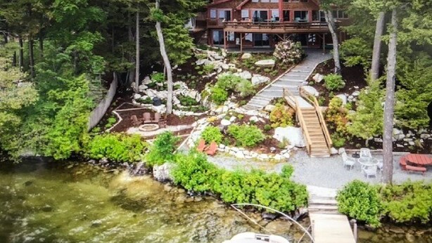 A house with a deck, surrounded by trees and a small garden. - Stunning Waterfront Home with Boat Dock, swim, boating. Bike & skiing nearby. (Moultonborough)