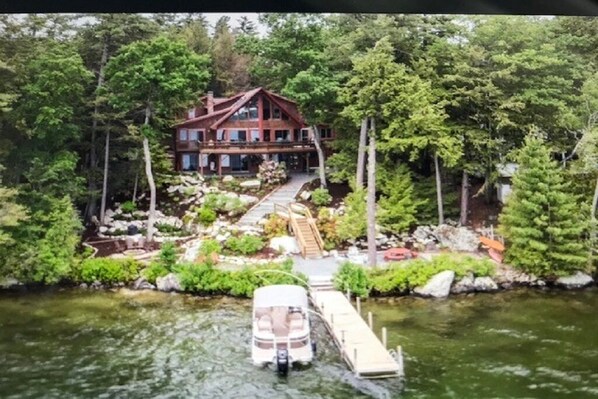 A cabin with a dock extending into a lake, surrounded by dense forest. - Stunning Waterfront Home with Boat Dock, swim, boating. Bike & skiing nearby. (Moultonborough)