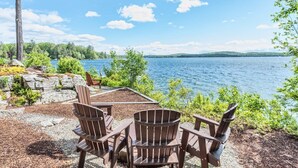 A lakeside seating area with Adirondack chairs and a stone fire pit. - Stunning Waterfront Home with Boat Dock, swim, boating. Bike & skiing nearby. (Moultonborough)