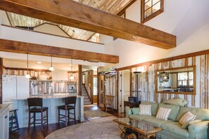A spacious kitchen with a central island, wooden beams, and a dining area with a green sofa and striped pillows. - Come enjoy Cribb Cove with family and friends! (Arapahoe)