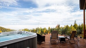 A wooden deck with a hot tub, lounge chairs, and a view of a forested area. - The Arial cottage, spectacular view and Spa (La Malbaie)