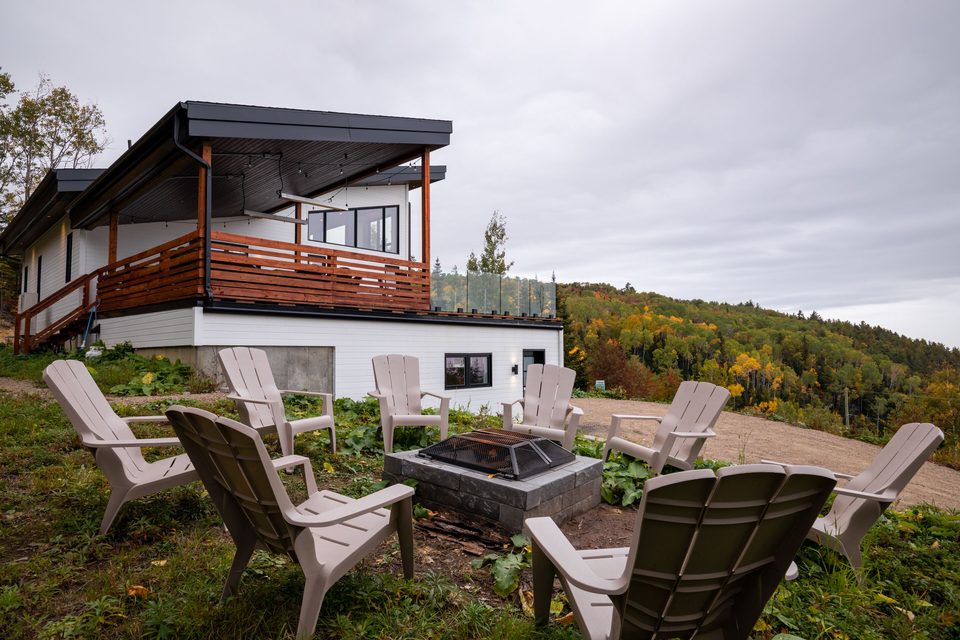 Ein modernes Haus mit Terrasse, Sitzgelegenheiten im Freien und einem Feuerkorb.