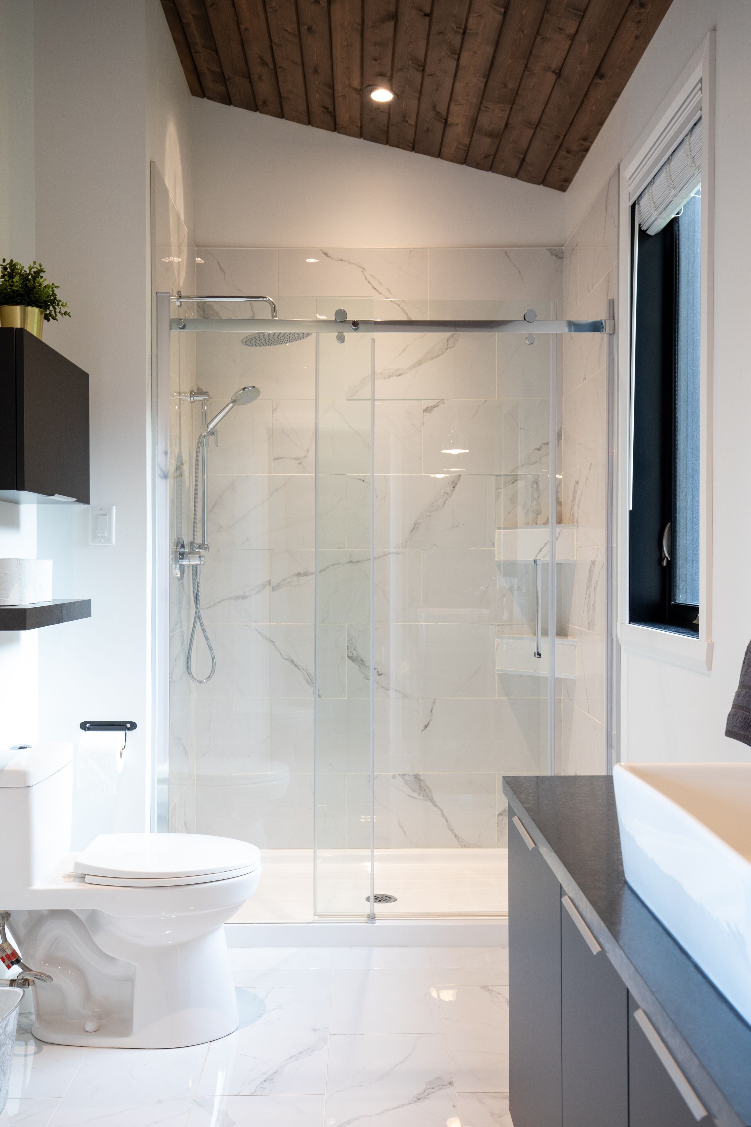 Ein modernes Badezimmer mit einer gläsernen Duschkabine, einer weißen Toilette und einem Boden aus Marmorplatten.