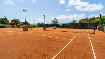 Un court de tennis avec un filet, entouré d’arbres et sous un ciel dégagé.