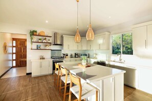 Une cuisine moderne avec des meubles blancs, un grand îlot central et des luminaires suspendus.