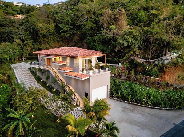 Une maison moderne avec un toit en tuiles de terre cuite, un escalier menant à un balcon et un jardin luxuriant.