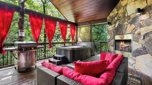A covered outdoor area with a stone fireplace, a grill, and wicker furniture. - Love Me Smore in Hochatown/Broken Bow,OK (Broken Bow)