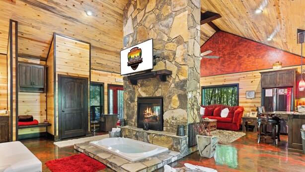 A log cabin interior with a stone fireplace, a red sofa, a white bench, and a stone wall. - Love Me Smore in Hochatown/Broken Bow,OK (Broken Bow)
