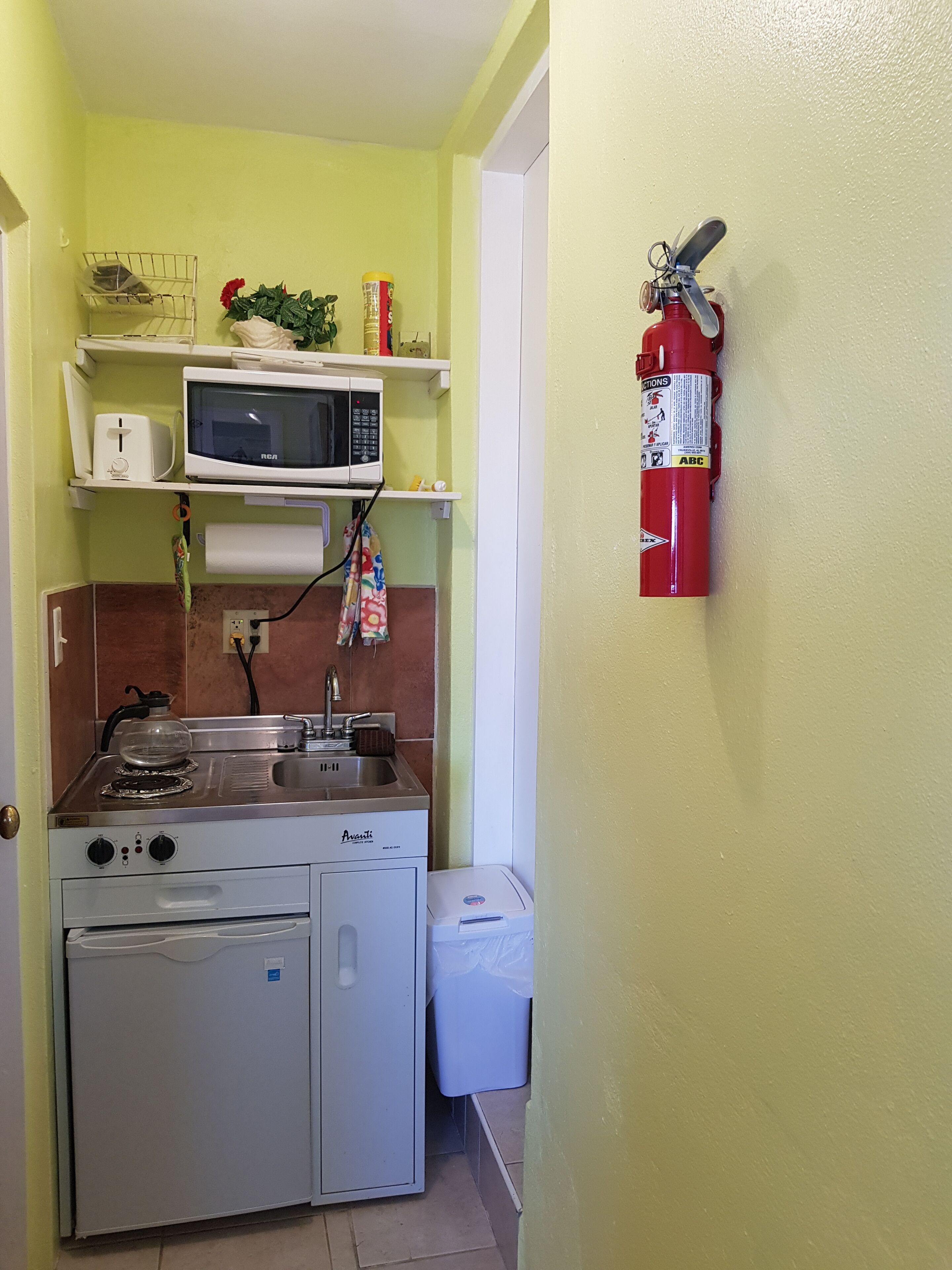 A compact kitchen with a microwave, stove, and sink. There is a fire extinguisher mounted on the wall.