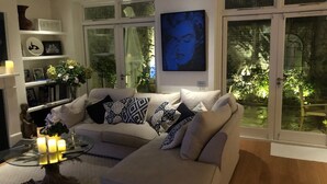 A modern living room with a beige sectional sofa, a glass coffee table, and a large window with a view of greenery.
