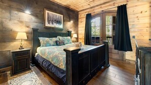 Een slaapkamer met houten lambrisering, een groot bed, een plafondventilator en een raam met gordijnen.