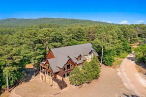 A large, two-story house with a stone foundation and a dark roof, surrounded by dense forest. - Majestic Mountain Lodge in Hochatown/Broken Bow, OK (Broken Bow)