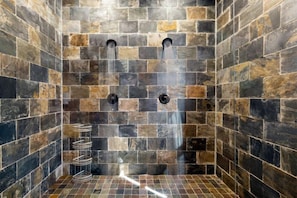 Shower area features a stone-walled enclosure with two water outlets and a towel rack.
