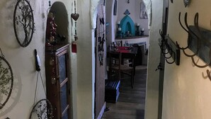 Een smalle gang met decoratieve wanddecoraties, een houten deur en een kleine tafel met stoelen op de achtergrond.