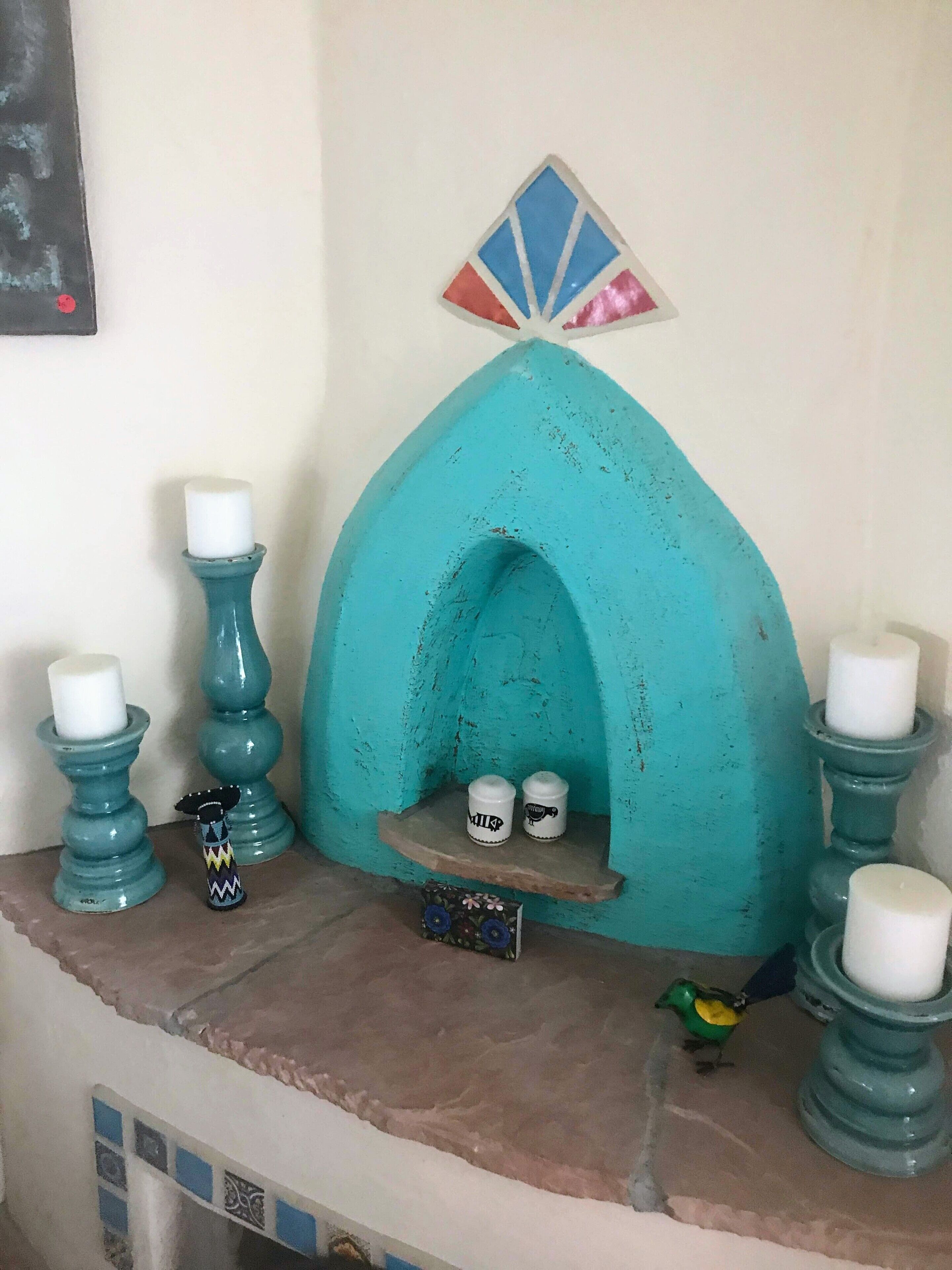 A teal-colored fireplace with white candles, a small shelf with salt and pepper shakers, and a decorative bird figurine.