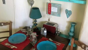Een eettafel gedekt met blauwe borden, bestek en een glas water. Er ligt een rode placemat, een blauwgroene lamp en een vintage radio op de tafel.