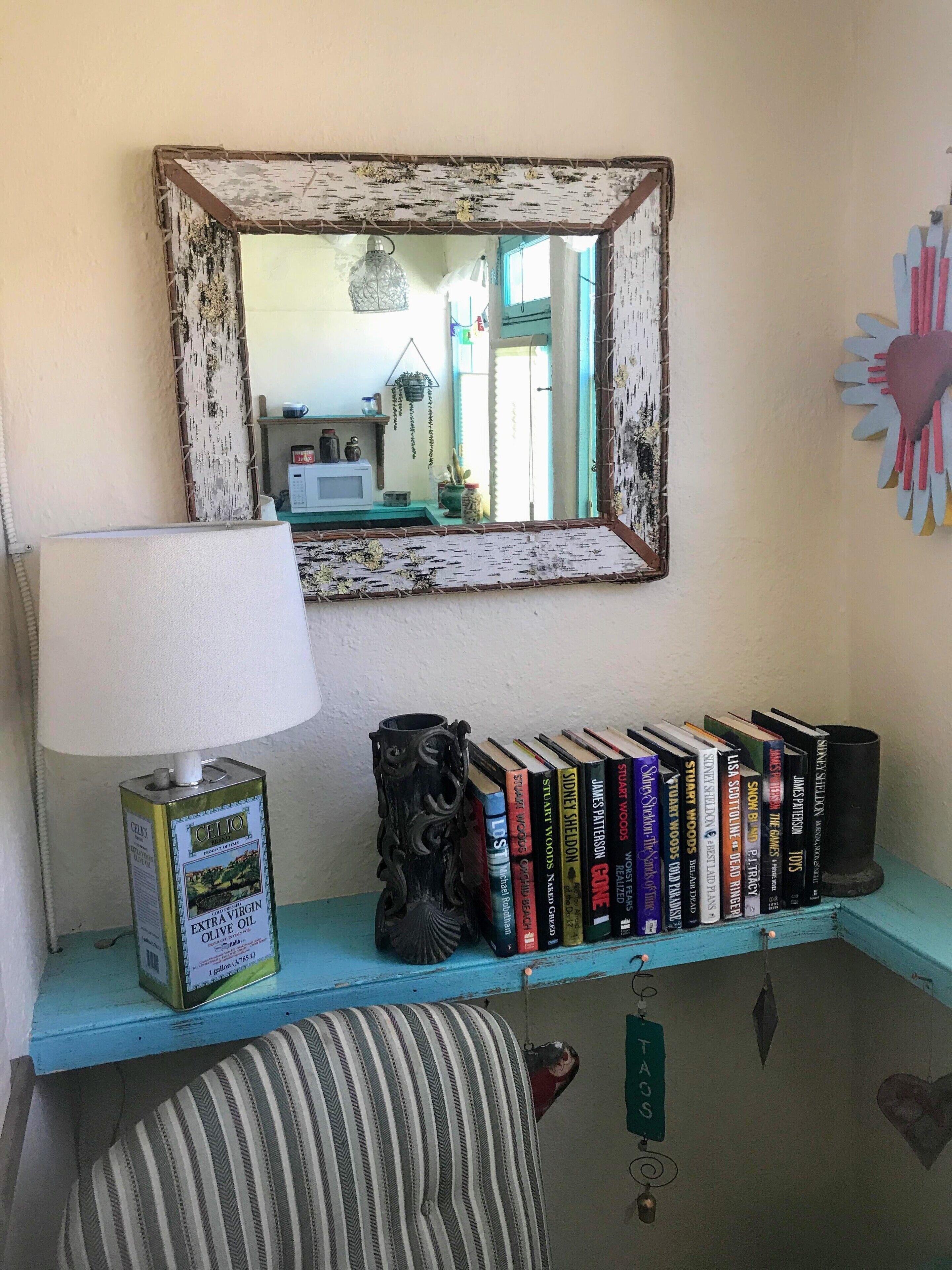 Una habitación con un espejo, una lámpara, un estante con libros y un cojín a rayas.