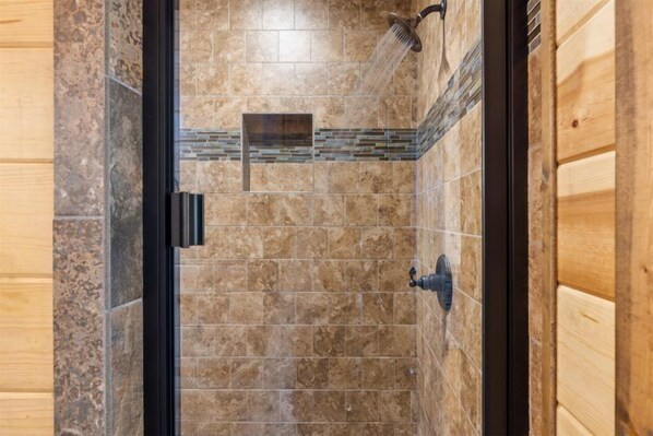 Ducha con puerta de cristal, paredes de azulejos y un panel de madera en un lateral.