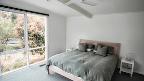 A bedroom with a large window, a bed with grey bedding, two bedside tables, and a view of trees outside.
