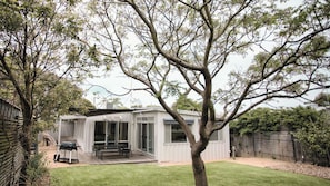A modern house with a patio, a tree in the foreground, and a fenced backyard.