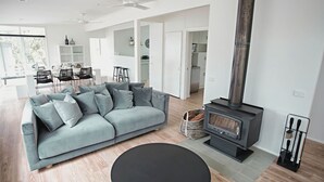Ein modernes Wohnzimmer mit grauem Sofa, einem runden schwarzen Tisch, einem Kamin und einem Essbereich mit Stühlen und Tisch.