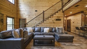 Ein Holzblockhaus-Interieur mit einem Ecksofa, einem Couchtisch und einer Treppe.