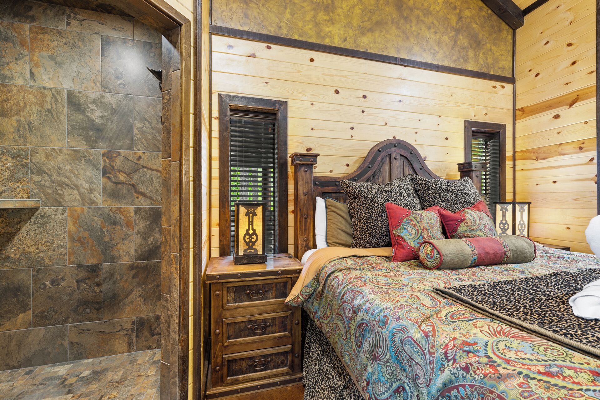 A bedroom with a wooden headboard, a patterned bedspread, and a nightstand with a lamp.