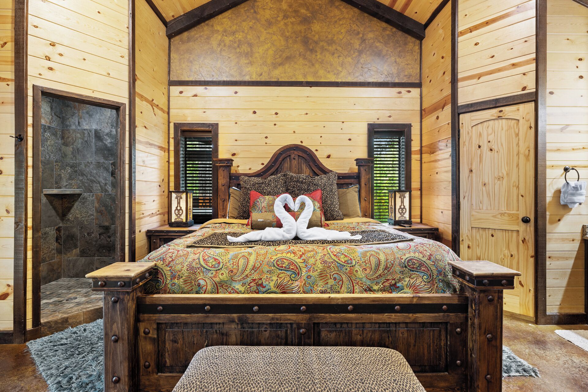 A wooden cabin bedroom with a bed, a nightstand, a bench, and a door.