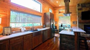 A modern kitchen with wooden walls, a large window, and a stone fireplace.