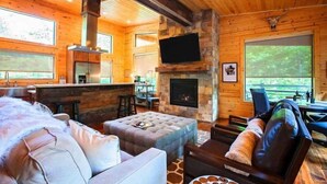 A log cabin interior with a fireplace, a bar area, and a seating area with a sofa and ottoman.