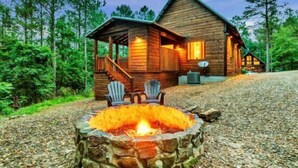 Eine Blockhütte mit einem Steinkamin, zwei Adirondack-Stühlen und einer Veranda.