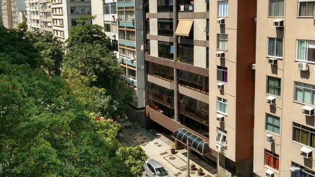 Een meerlaags woongebouw met balkons, een overdekte parkeerplaats en een straatbeeld.