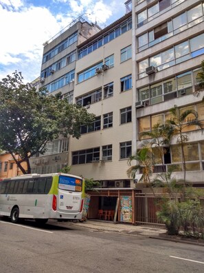 A multi-story building with large windows and air conditioning units. A bus is parked in front of the building.