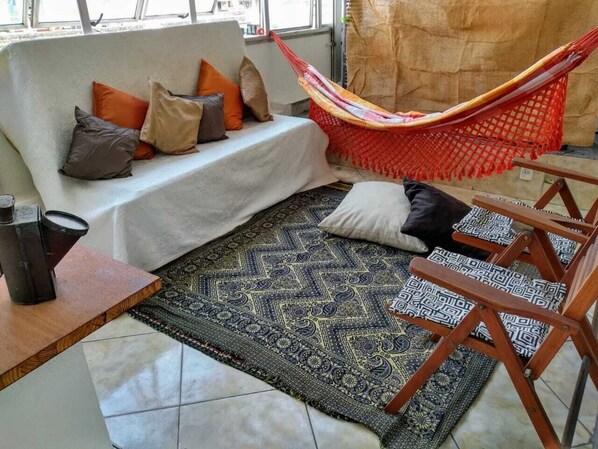 A cozy living area with a sofa, cushions, a hammock, a patterned rug, and a small wooden table.