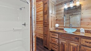 Baño de una cabaña de madera con bañera, lavabo de vidrio y un espejo grande.